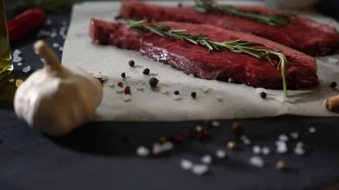 Close up view of raw beef steak on table while adding salt with pepper and Stock Footage 115831675