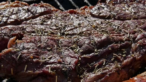 Close view of raw beef steak on a BBQ grill sizzling over flaming hot coals in a Stock Footage 150467172