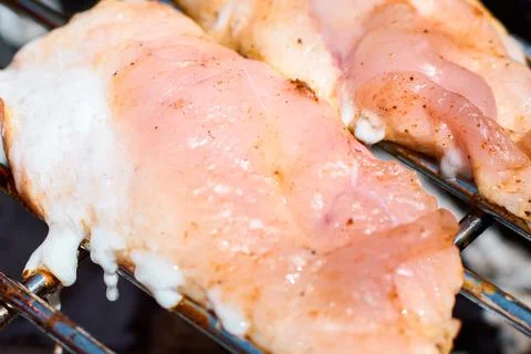 Close-up view of raw chicken meat cooking on a hot metal barbecue grill grate Stock Photos