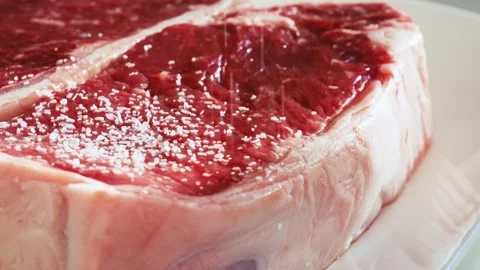 Close view of a raw new york steak being seasoned with salt in slow motion Stock Footage 258306876