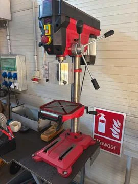A close-up view of a red and black drill press machine in a workshop Stock Photos