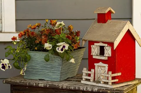 A close up view of a red hand made  farm house model placed next to a pot of  Stock Photos