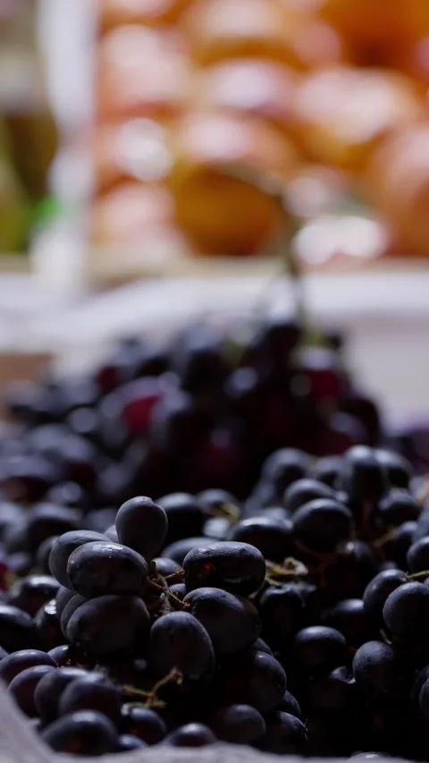 Close-up view of ripe black grapes piled on a market stall, with soft natural 库存影片 329555347