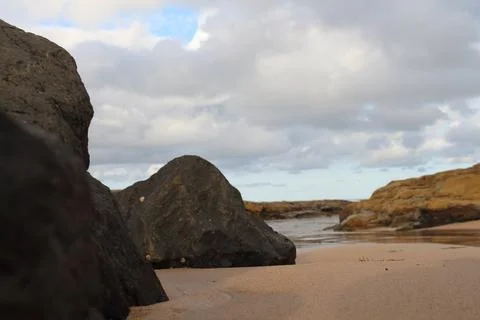 Close-Up View Of Rocky Beach With Sand And Large Boulders Under Cloudy Sky Stock Photos
