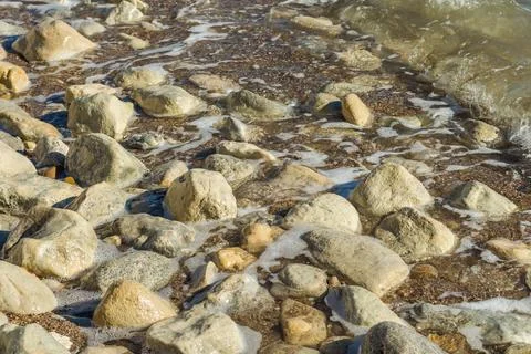 A close-up view of a rocky beach with waves gently washing over smooth, gray  Stock Photos