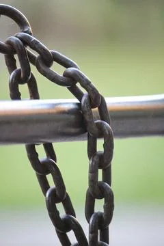 Close-up view of a rusty chain linked to a metal pole in a green outdoor se.. Stock Photos