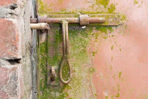 A close-up view of a rusty metal latch on a weathered brick wall with green Stock-Fotos