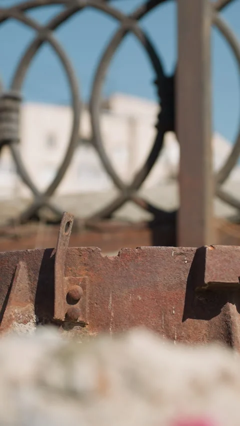 Close View of Rusty Metal Object with Ornate Fence and Urban Background Stock Footage 310335497
