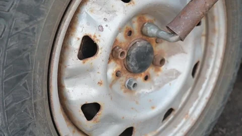 Close-up view of a rusty wheel rim with a tool engaged in removing a lug nut. Stockbeeldmateriaal 337550533