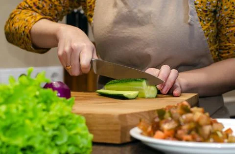 Close-up view of the salad preparation process. A woman in an apron cuts a Stock Photos