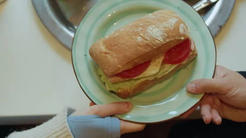 Close up view of sandwich held by two hands over table with matching plates and Stock Footage 344874284