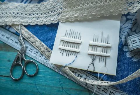 Close up view of scissors and set of stitching needles on linen fabric with l Stock Photos