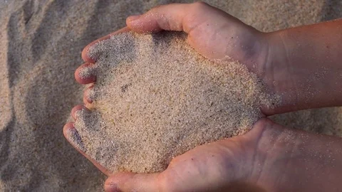 Close up view of sea sand running through a womans hands against a blurred ocean Stock-Footage 72652225