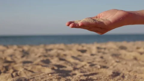 Close up view of sea sand running through a womans hands against a blurred ocean Stock Footage