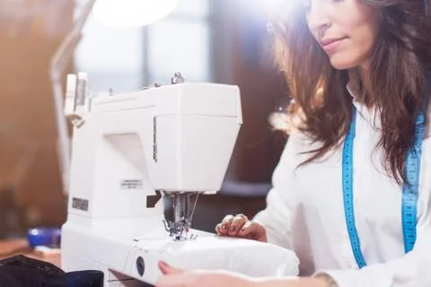 Close-up view of sewing machine and young female tailor working on it while Stock Photos