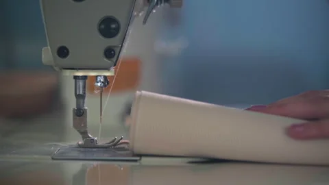 Close view of sewing machine needle and hands guiding rolled fabric on worktable Stock Footage 321887331