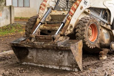 Close view shows a compact, dirty skid steer loader with a front-end bucket Stock Photos
