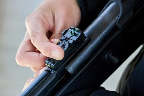 Close-up view shows hand adjusting fiber optic rear sight on rifle. Finger tu Stock Photos