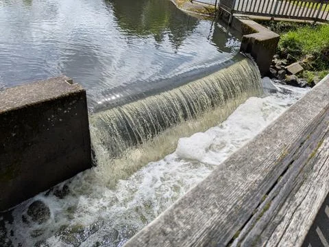 A close view shows a man-made waterfall cascading from a pond into a river Stock-Fotos