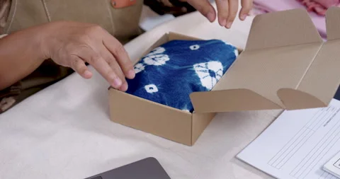 Close view shows senior asian seller tucks blue shibori fabric into parcel box, Stock Footage 339007180