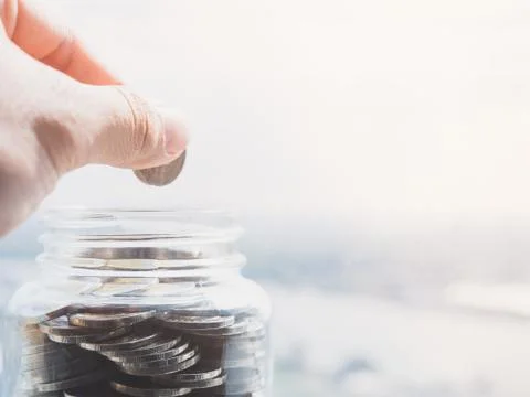 Close up view on the side of the hand holding a coin to put money in a glass Stock Photos