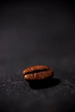 Close-up view of a single coffee bean lying on a dark stone surface Foto stock