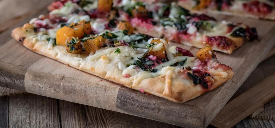 A close up view of slices of root vegetable flat bread pizza ready for eating. Stock Photos