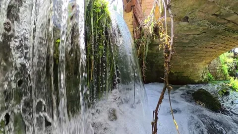 Close-up view of a small waterfall under a small stone bridge Stock Footage 338348358