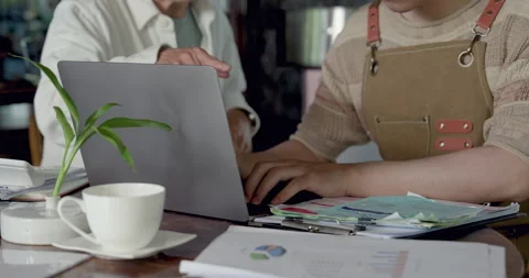 Close view of son using laptop beside cafe paperwork, father nearby supporting 動画素材 333455933