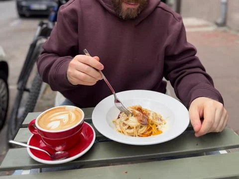 Close view of spaghetti lifted on fork beside latte in red cup at an outdoo.. Stock Photos