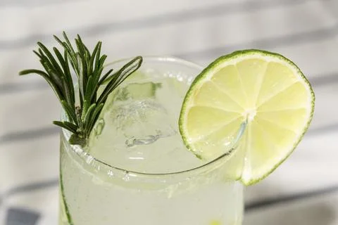 Close view of sparkling lime drink with rosemary and ice in clear glass, brig Stock Photos