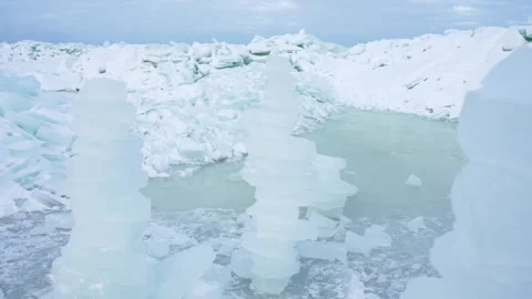 Close view of stacked ice columns beside a meltwater pool and broken sea-ice Stock Footage 332046647