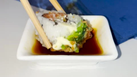 A close up view of a sushi roll being held with chopsticks and dipped into a Stock Footage 282137020