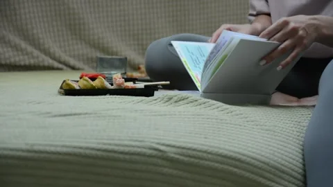 Close-up view of sushi rolls, an open notebook, and the hands and legs Vídeo Stock 347155652