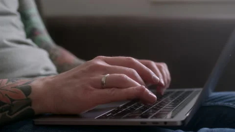 Close up view of tattooed man working on laptop while sitting on sofa at home Stock Footage 233329492