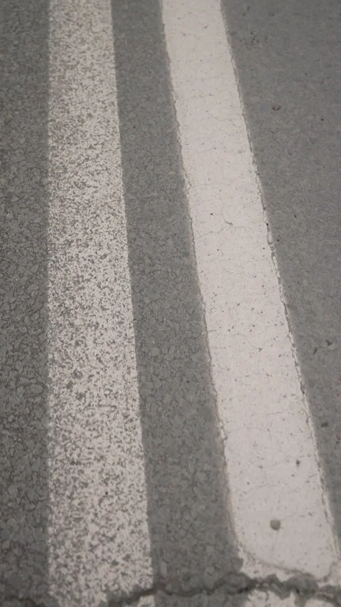 Close-up view of textured asphalt road surface featuring parallel white painted Stock-Footage 312674755