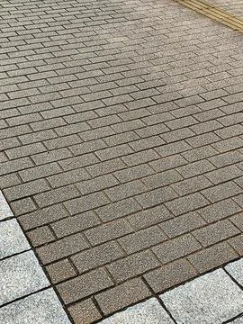 Close-up view of a textured brown brick sidewalk bordered by light concrete e Stock Photos