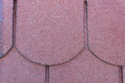 Close-up view of a textured red roofing shingle, showcasing its unique shape and Foto stock
