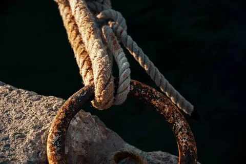 Close up view of thick rope tied securely to a rusty iron mooring ring Stock Photos