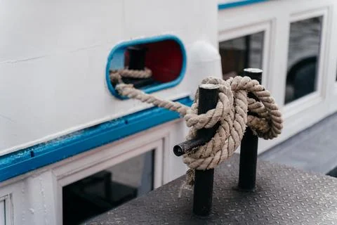 A close-up view of a thick rope tied securely around a metal bollard, fastening Stock Photos