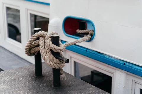 A close-up view of a thick rope tied securely around a metal bollard, fastening Stock Photos