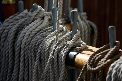 Close up view of thick ropes secured to wooden belaying pins along a deck rai Stock Photos