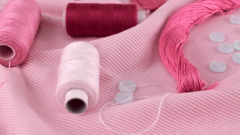 Close-up view of the thin pink cotton jersey, buttons and spools of threads. Stock Footage 290811061