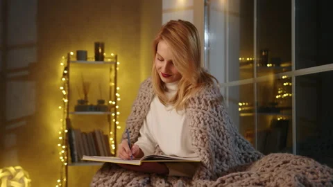 Close-up view of a thoughtful, blonde-haired lady filling hear diary Stock Footage 229535174