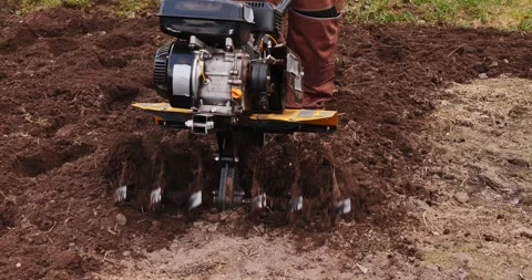 Close-up view of a tiller machine with a powerful engine digging, spinning, and 스톡 동영상 333232652