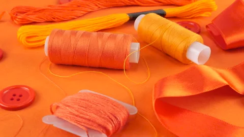 Close-up view of tufts orange cotton fabric, buttons and spools of threads Stock Footage 290802033