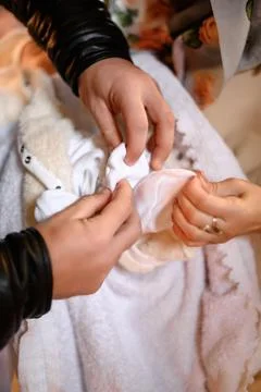 Close-up view of two adults gently dressing a baby in soft, white garments. T Foto stock