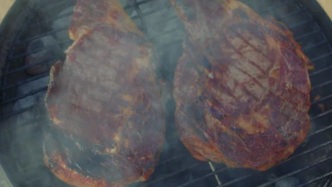Close up view of two cooked ribeye steaks about to be removed from the grilling  Vídeo Stock 285469391