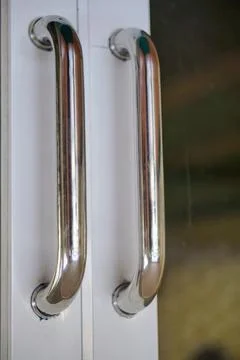 Close-up view of two shiny stainless steel metal door handles installed Stock Photos