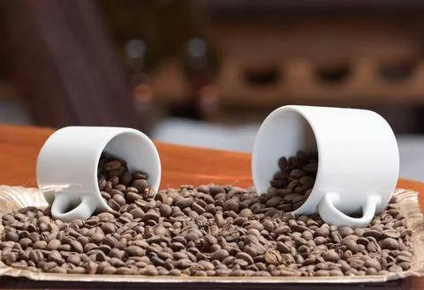 Close view of two white cups on their sides with coffee beans spilling out of it Stock Photos
